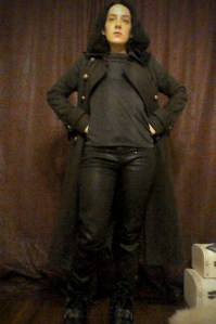 The Bridge Saga Khaki Next military style coat, dark top, wax coated black trousers and leather biker boots